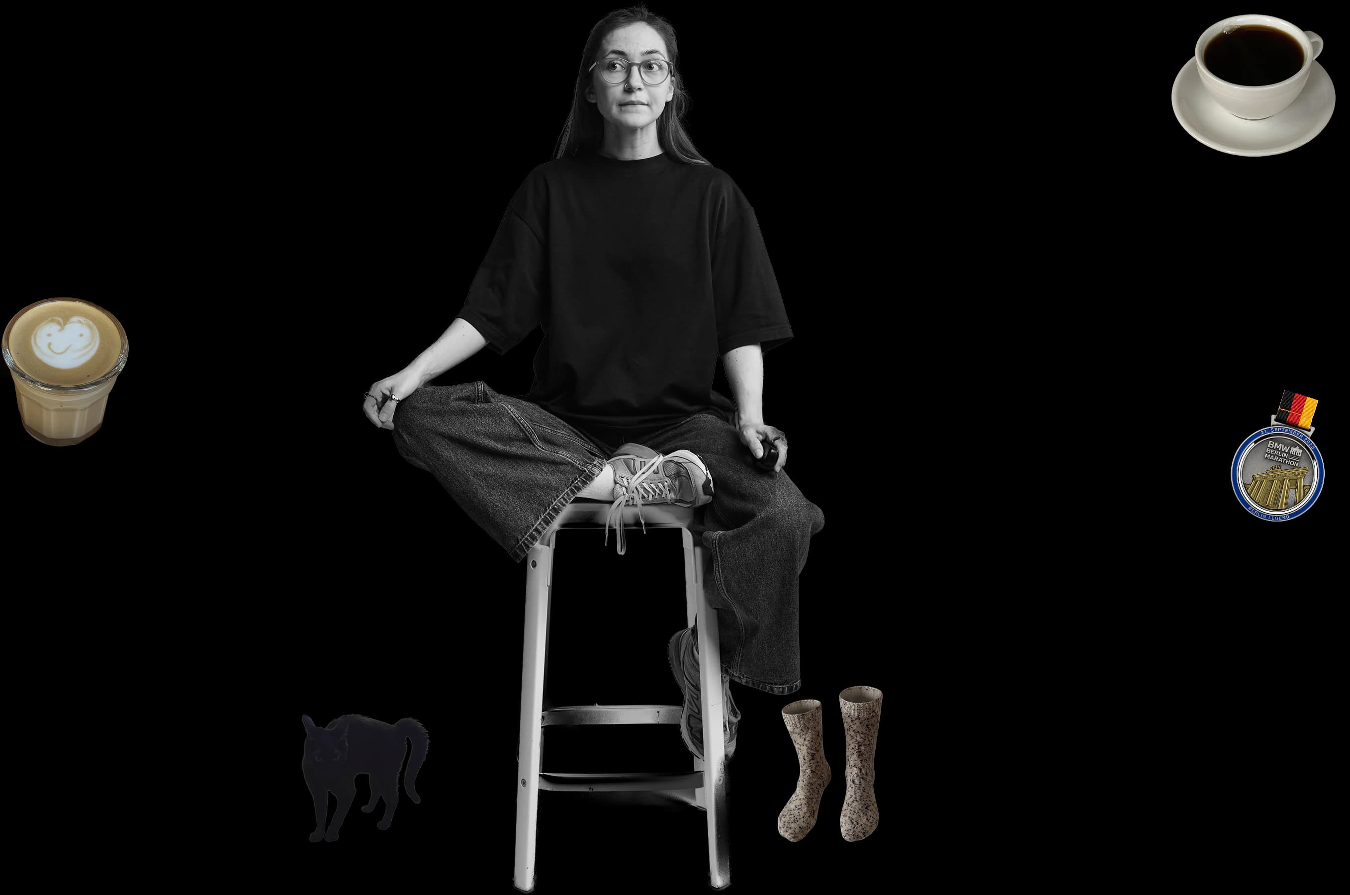 Viktoriia sitting on a stool, surrounded by a latte, a cup of black coffee, her Berlin Marathon medal, her black cat Luna and hand-knitted socks
